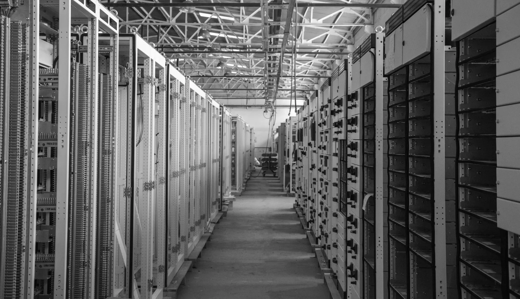 Rows of switchgear cabinets down a factory hall, in black and white